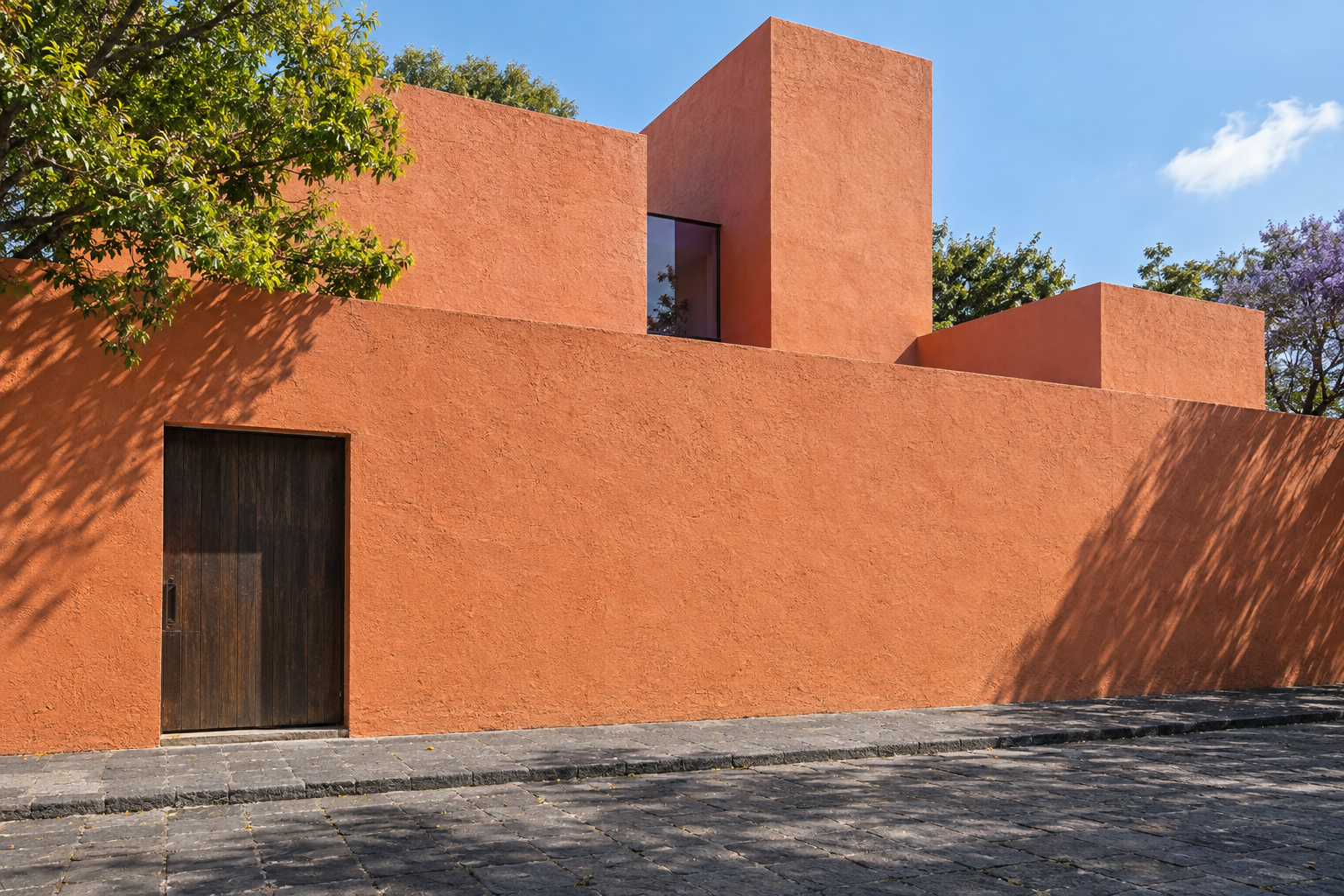 Wide exterior facade of Luis Barragán's Casa Gilardi on an urban street in Mexico City, showing planar masonry walls, a warm timber door, and morning sidelight.