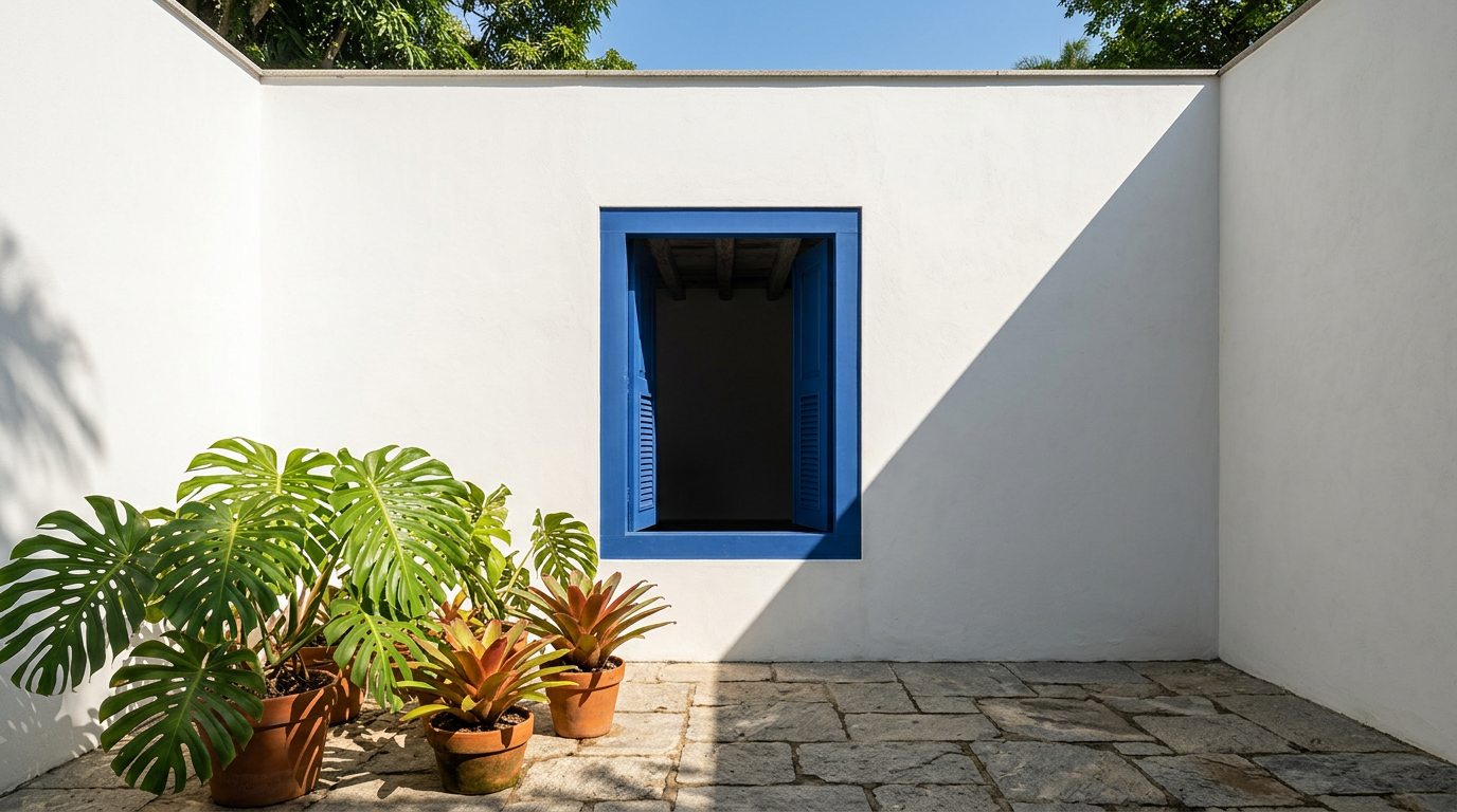 White plastered walls and stone paving enclose a patio with a vivid blue window and potted tropical plants.