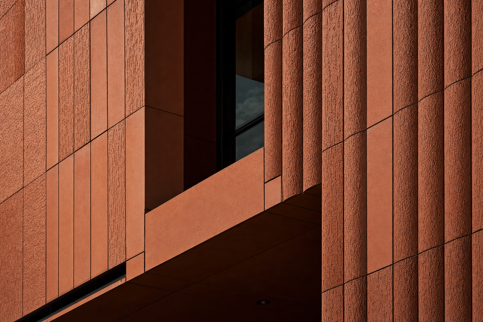 A close-up view of a modern building's facade, featuring textured terra cotta panels arranged in a rectilinear pattern, illuminated by natural light.