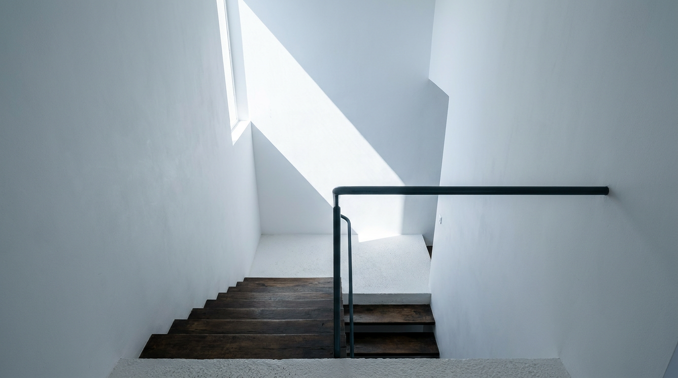 Modern interior concrete and white walls with timber stairs and a dark metal handrail from an elevated perspective.
